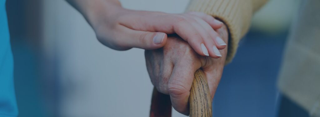 Une personne pose sa main sur celle d’une personne âgée tenant une canne